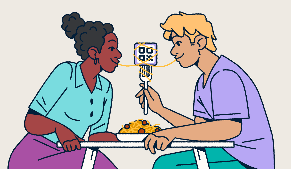 A couple sitting at a table sharing a bowl of spaghetti and meatballs. One partner is holding a fork with a QR Code on it and a piece of spaghetti wrapped around it. They each have one end of the noodle in their mouth.