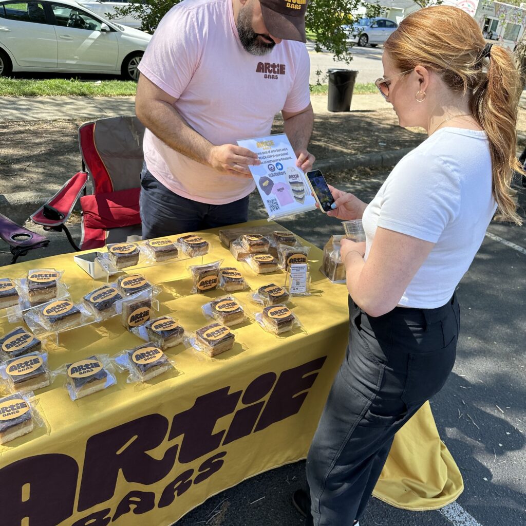 Artie Bars founder holding up a Bitly QR Code for a customer to scan with their phone.