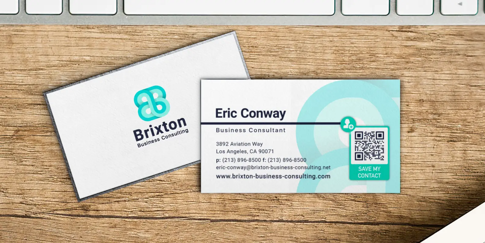 The front of a business card and the back of a business consultant's business card with contact information and a QR Code on it lying on a wooden desk.