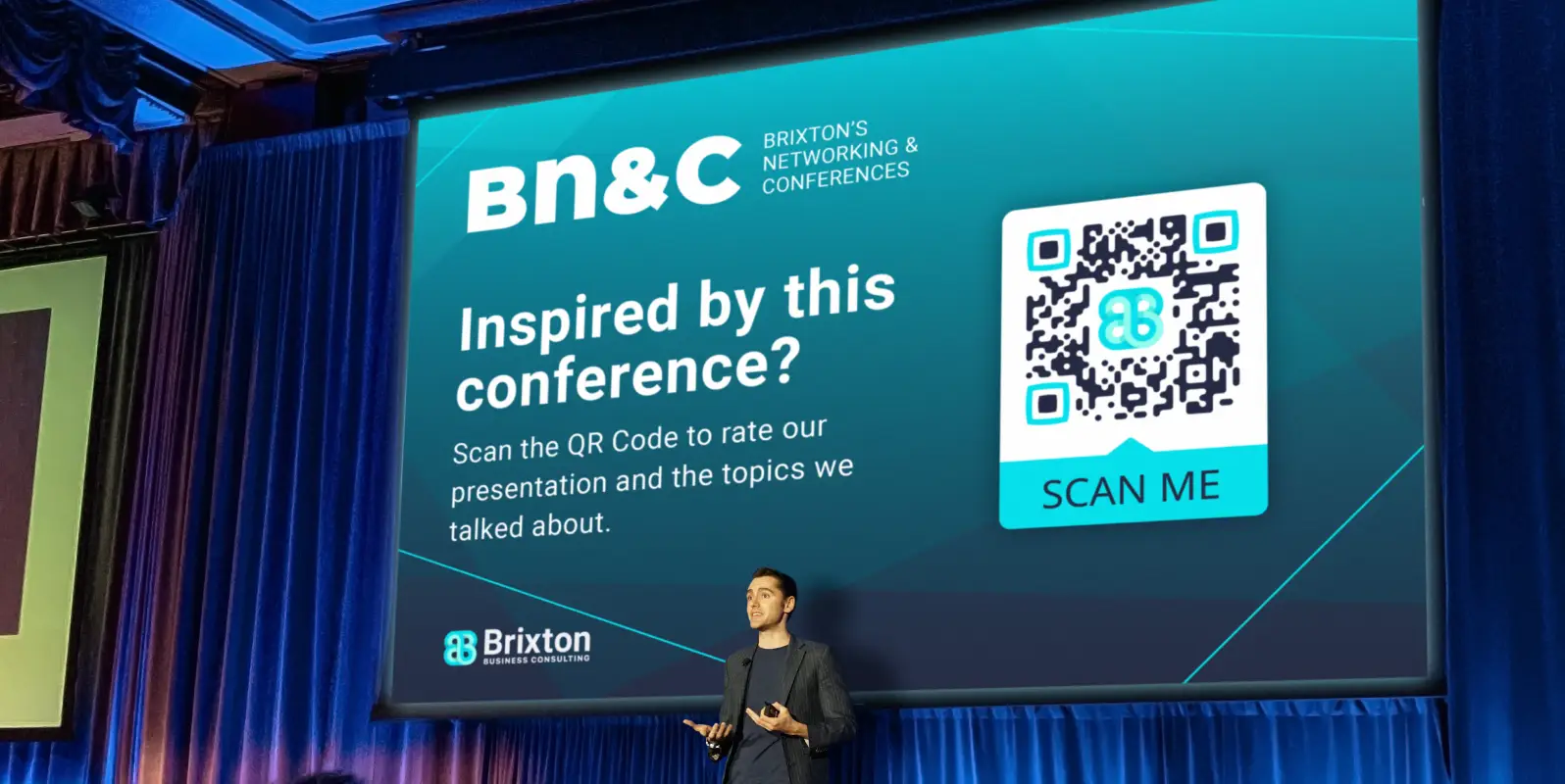 A man presenting at a conference in front of a projector screen. The screen shows a QR Code that allows scanners to rate the presentation.