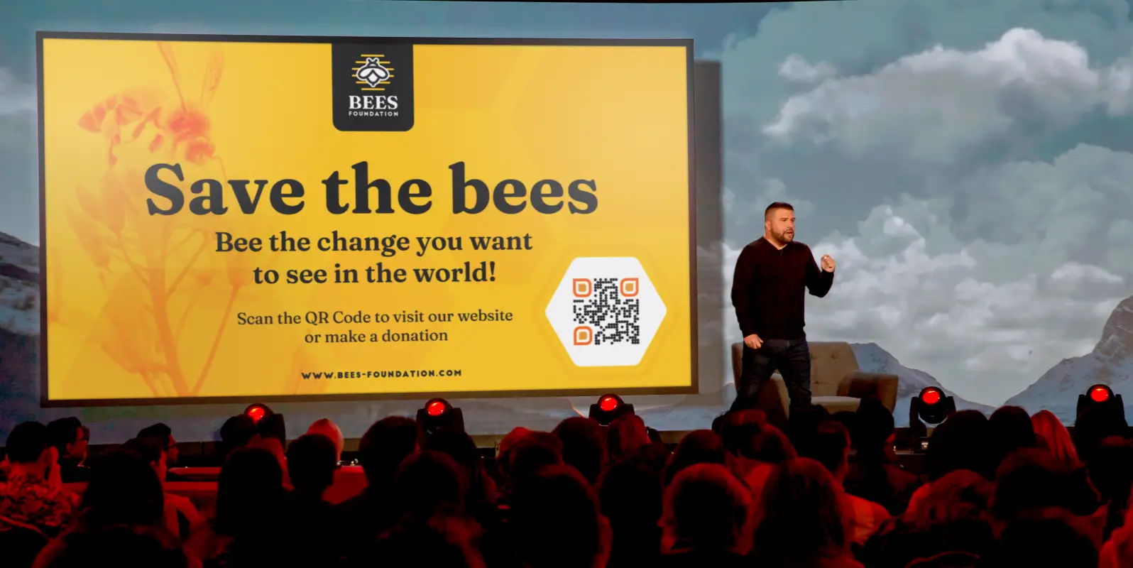 A man giving a presentation at a nonprofit event. A QR Code for donations is on screen.